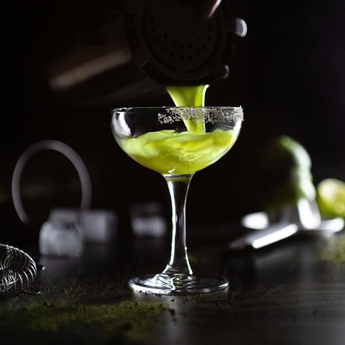 pouring the matcha margarita from a cocktail shaker into the matcha salted coupe glass.