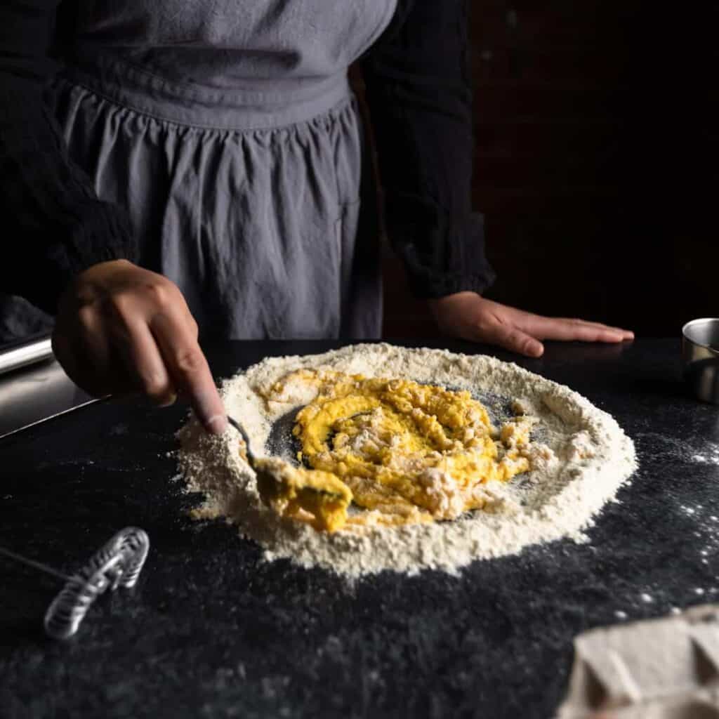 an aproned woman whisking eggs into semolina and bread flour to make fresh semolina pasta dough