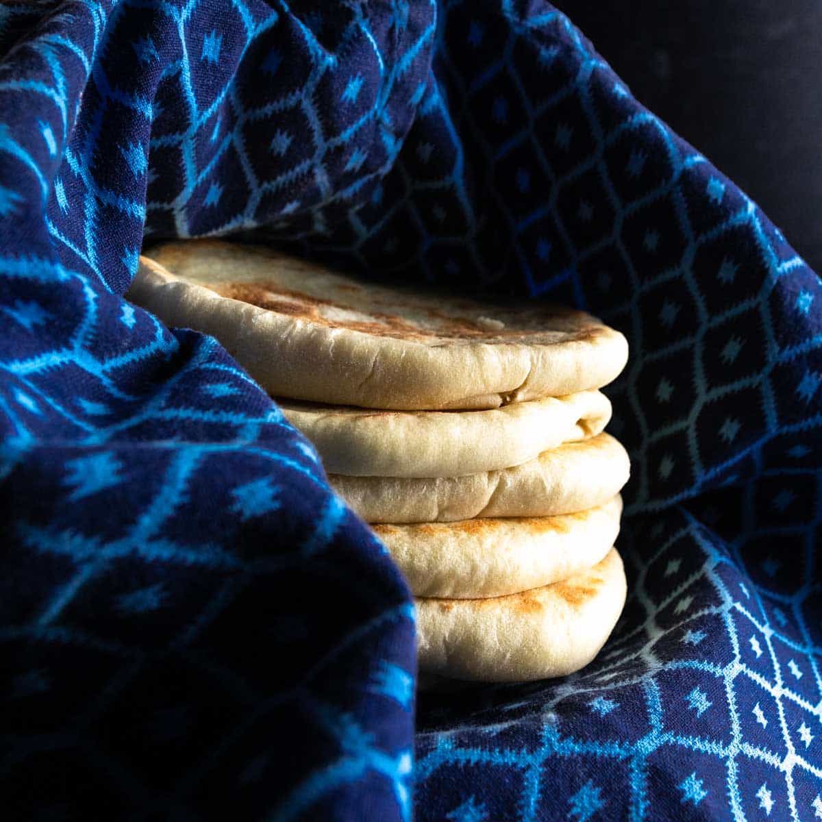 A stack of pita pockets wrapped in a clean dish towel to steam after baking