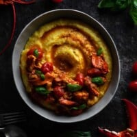 close up overhead view of a bowl with a crescent of Maine lobster cooked with saffron, blistered cherry tomatoes and a rich lobster stock over a swirl of creamy grits