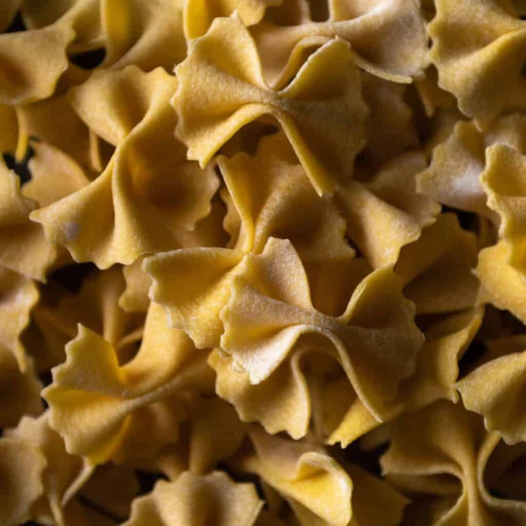 A close-up macro shot of a pile of fresh made farfalle from homemade semolina pasta dough