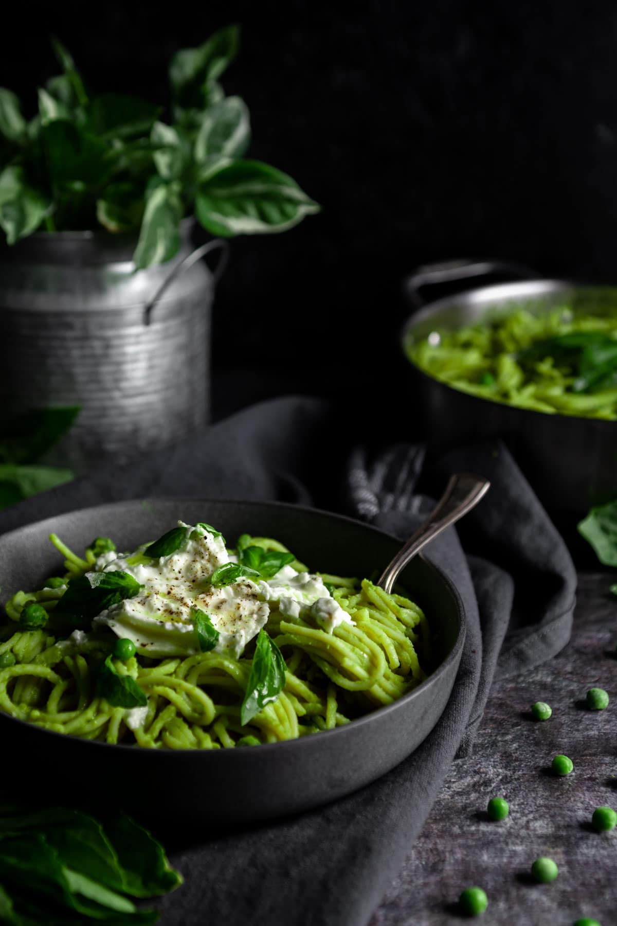 Bowl of Green Pea Pasta topped with burrata cheese in bowl surrounded by green peas and a pothos plant