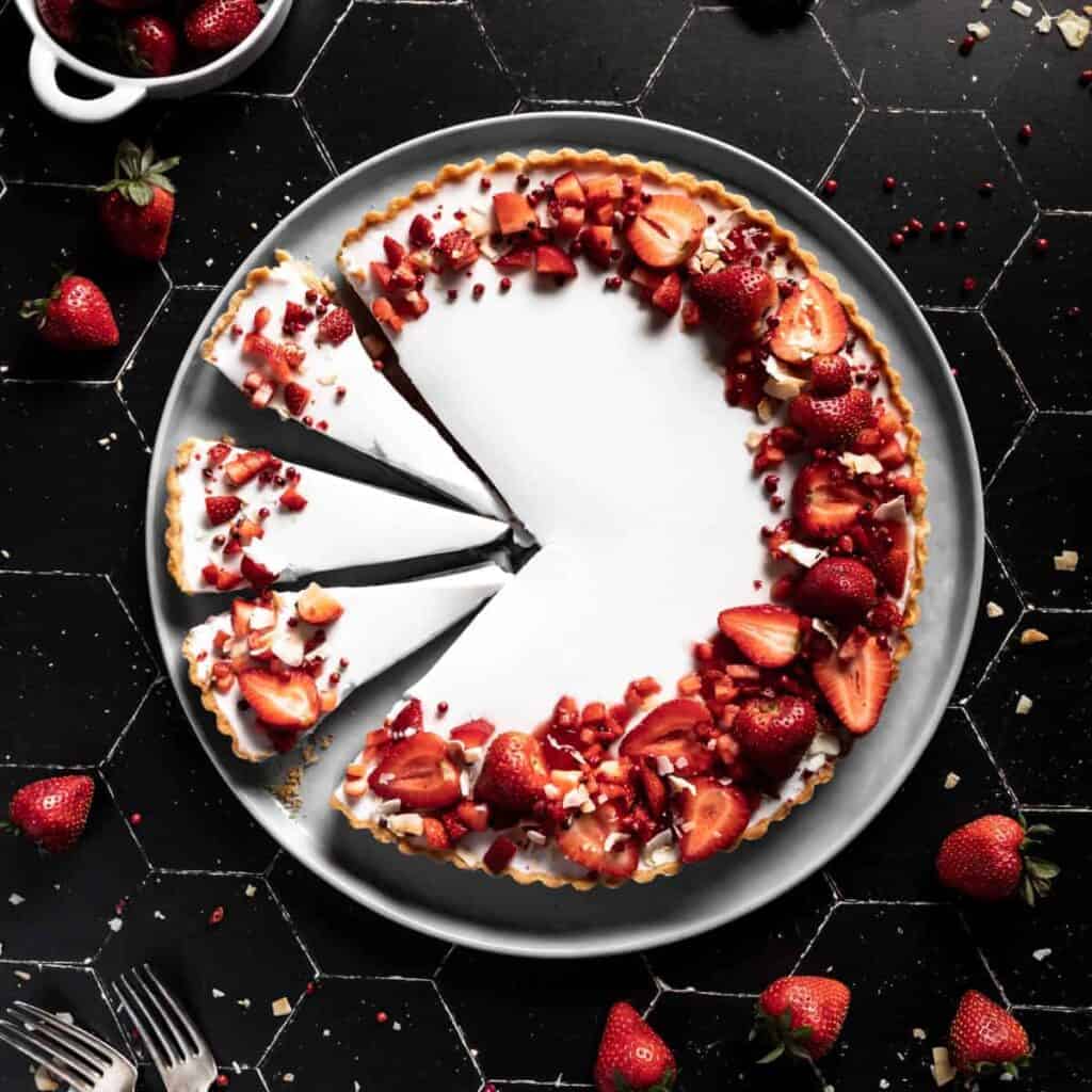A coconut panna cotta tart decorated with a crescent of strawberries and 3 slices cut