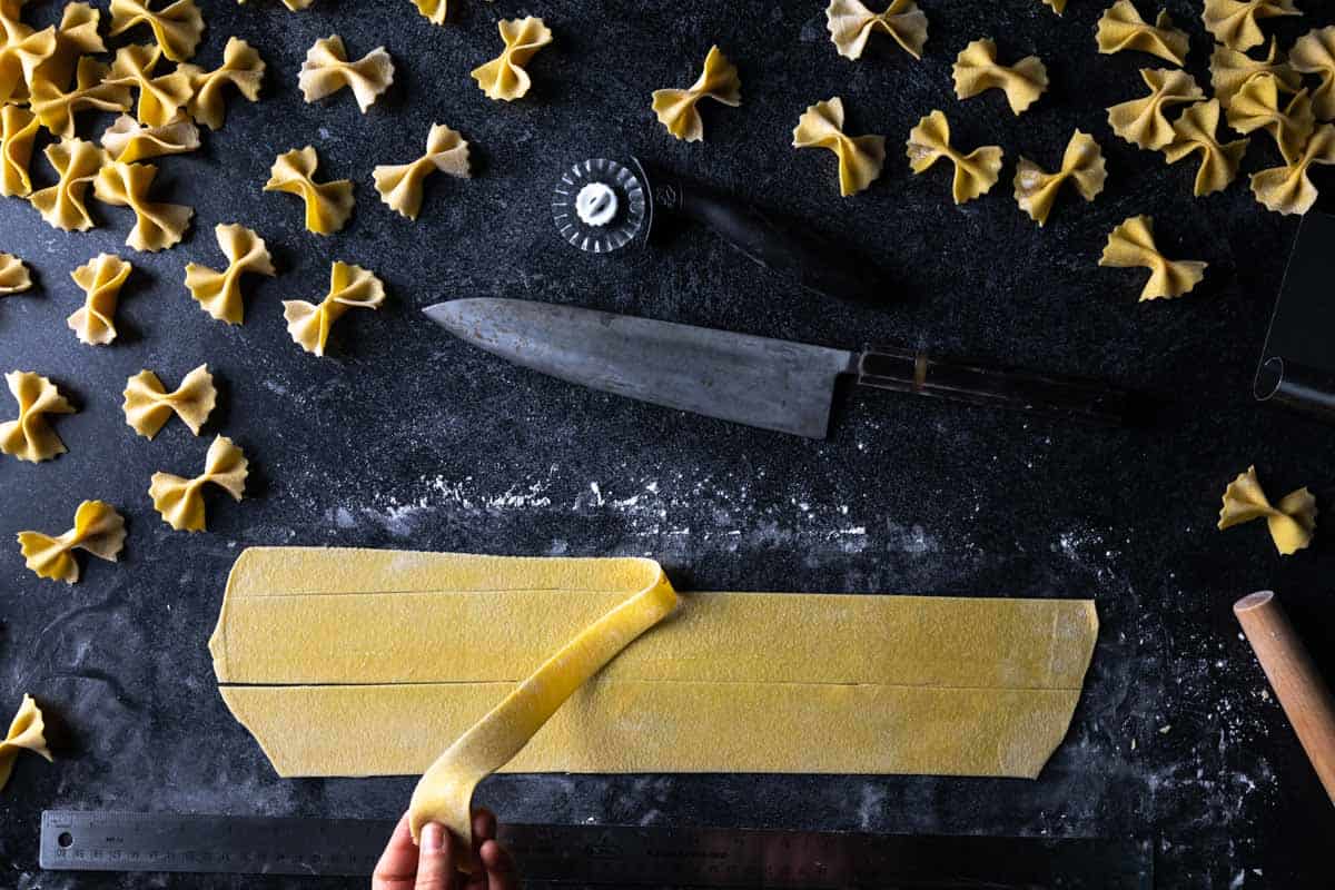 A hand pulling a way a scrap of semolina pasta dough away from a squared edge