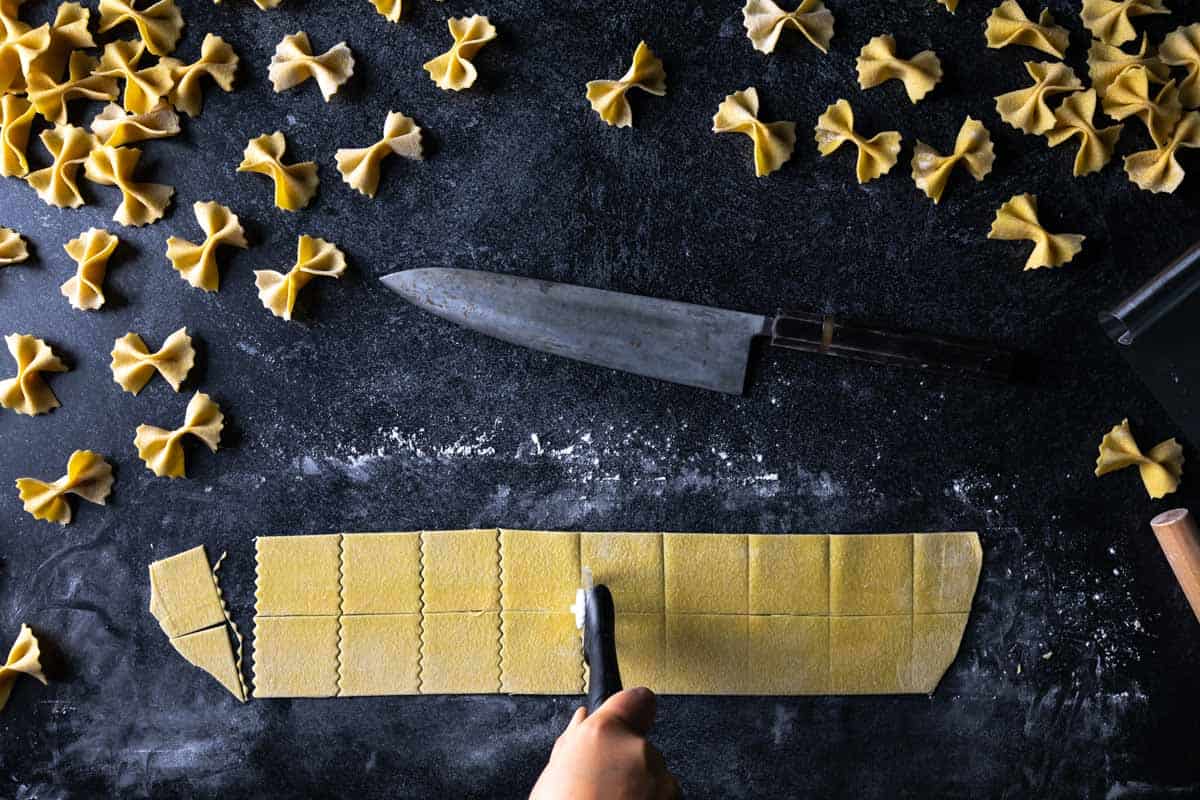 A fluted pastry wheel cutting squares of pasta dough