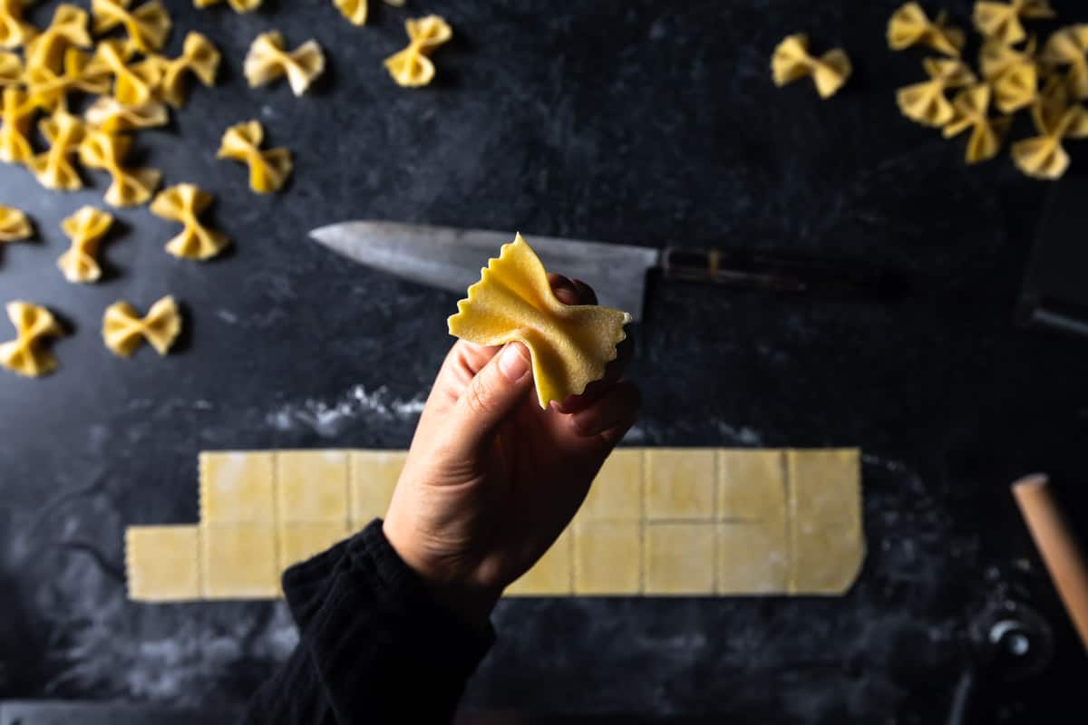 a hand pinching a square of pasta dough into a bowtie shape