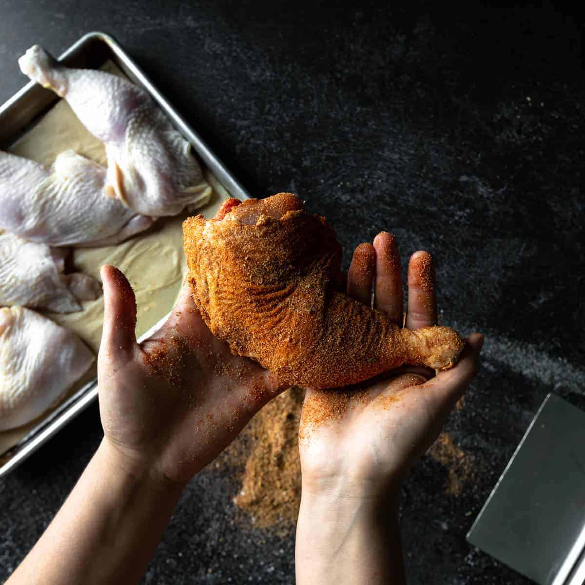 Hands holding a chicken quarter rubbed in a dry spice blend