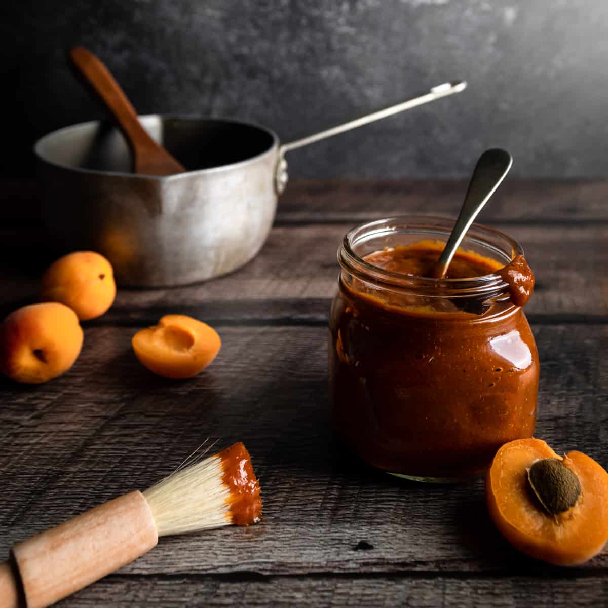 a jar or apricot bbq sauce bext to a pot, apricots and basting brush