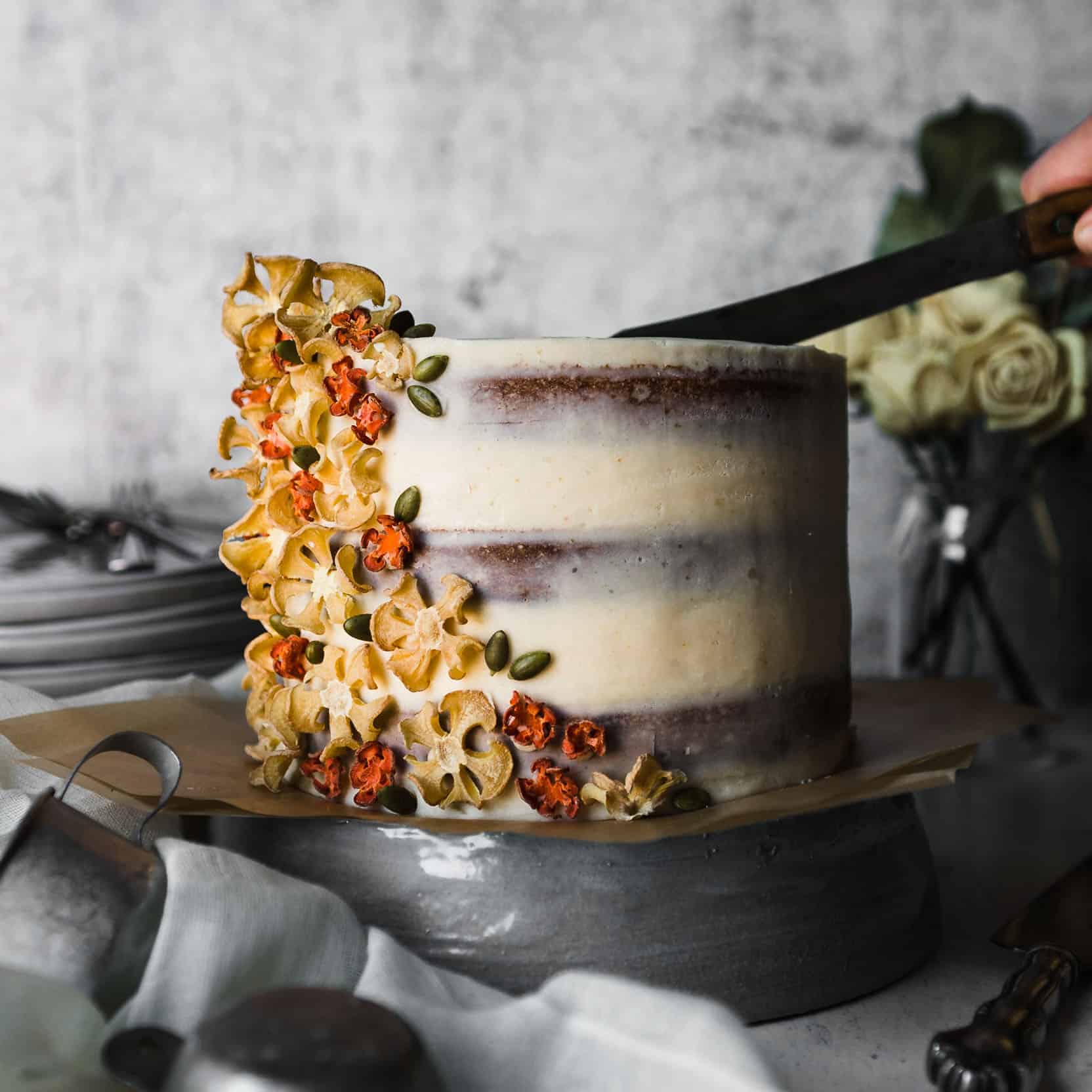 A knife cutting into a carrot spice cake that is semi-naked frosted with brown butter buttercream