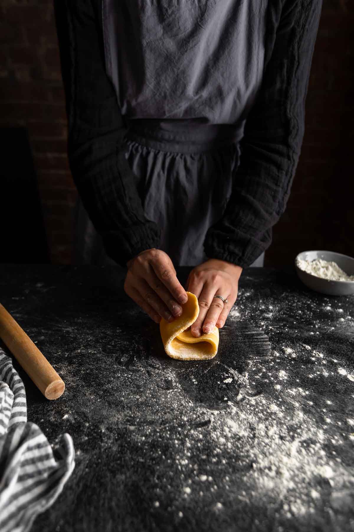 a woman folding an oval of pasta dough in thirds