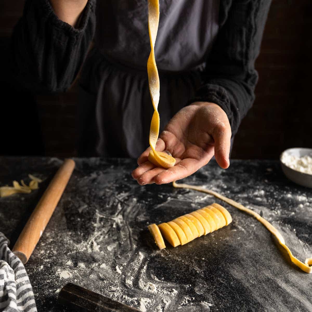 a woman unraveling a little ribbon of fettuccine pasta