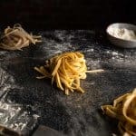 A nest of golden colored fettuccine noodles on a floured counter top