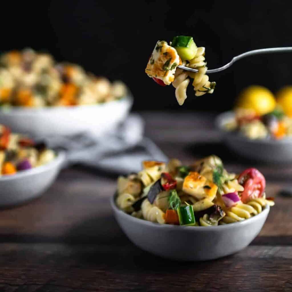 A forkful of halloumi pasta salad hovering over a small bowl