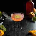 A peach daiquiri in a fluted coupe glass with a lime wheel garnish