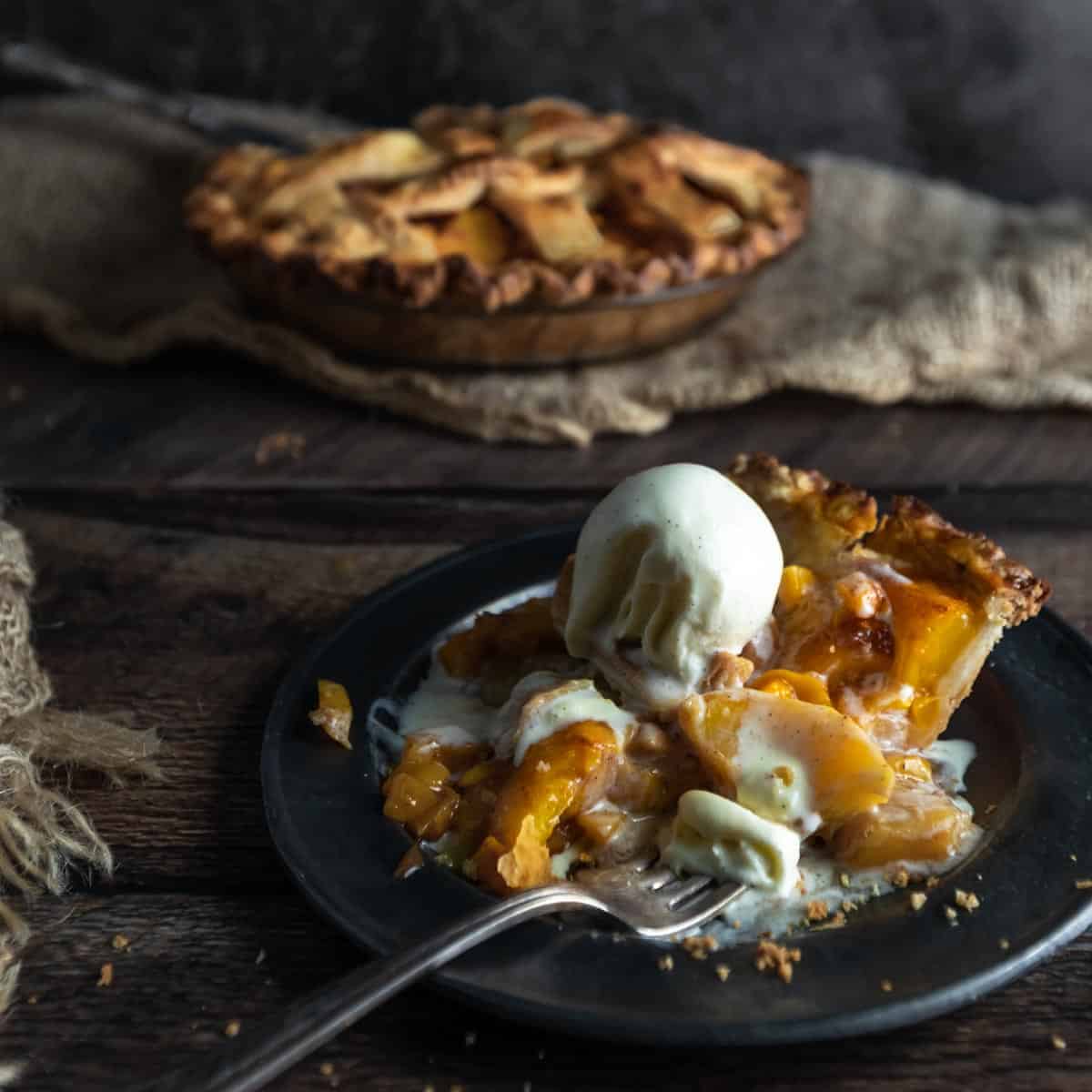 A scoop of vanilla ice cream melting into a slice of warm peach mango pie.