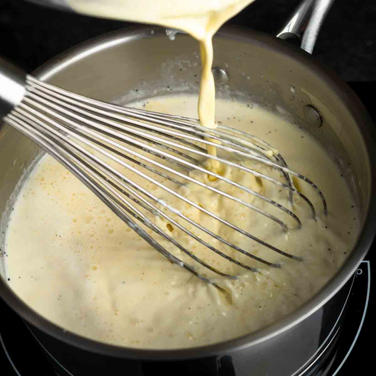 Pouring vanilla bean custard back into the pot while whisking