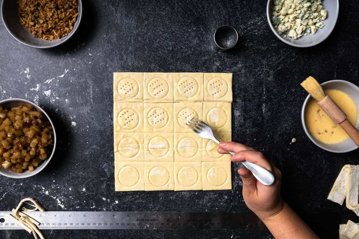 A hand holding a fork to poke holes in the center of each puff pastry square
