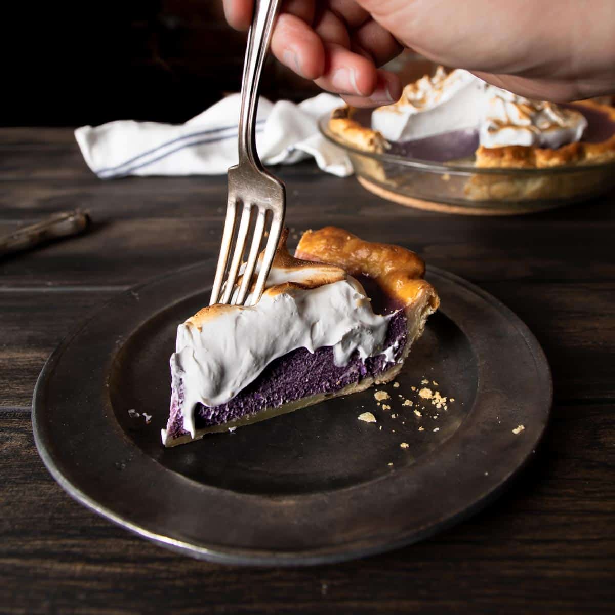 A hand holding a fork dipping into the first bite of purple sweet potato pie with Swiss meringue