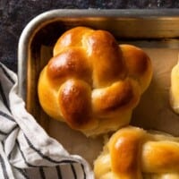 A close-up of a golden brown braided challah bun on a sheet tray