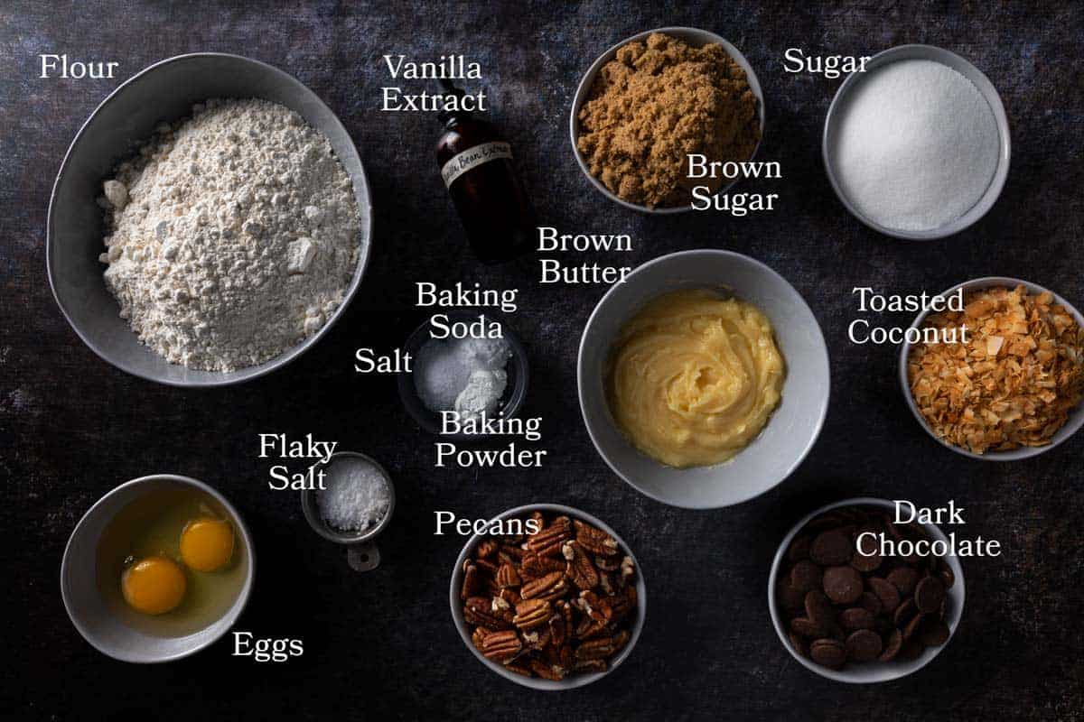 Ingredeints for this cookie recipe including flour, brown butter, sugar, brown sugar, baking powder, baking soda, salt, eggs, dark chocolate, pecans and toasted coconut