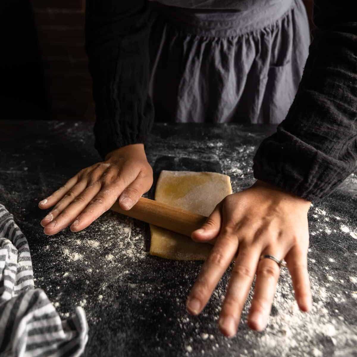 a woman rolling a piece of pasta dough into a long sheet