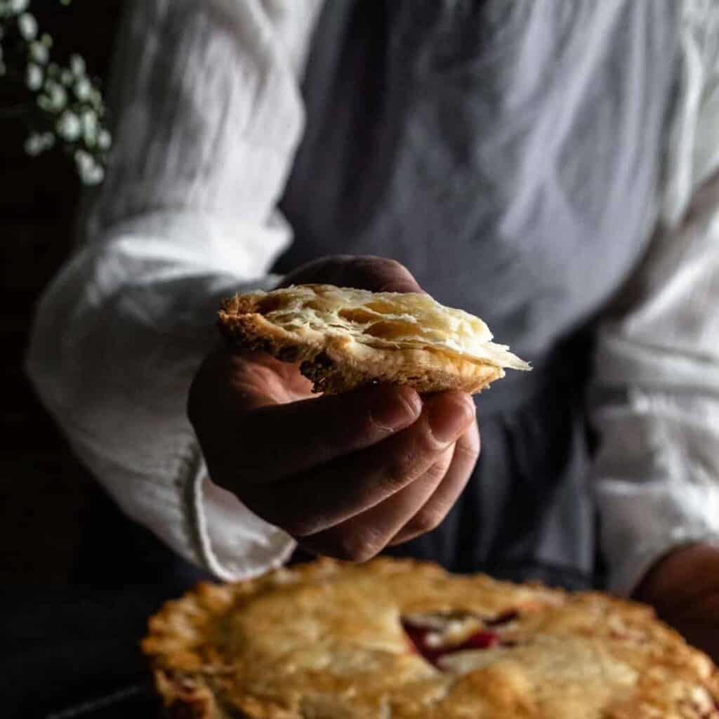 A woman holding a flaky piece of buttery pie crust