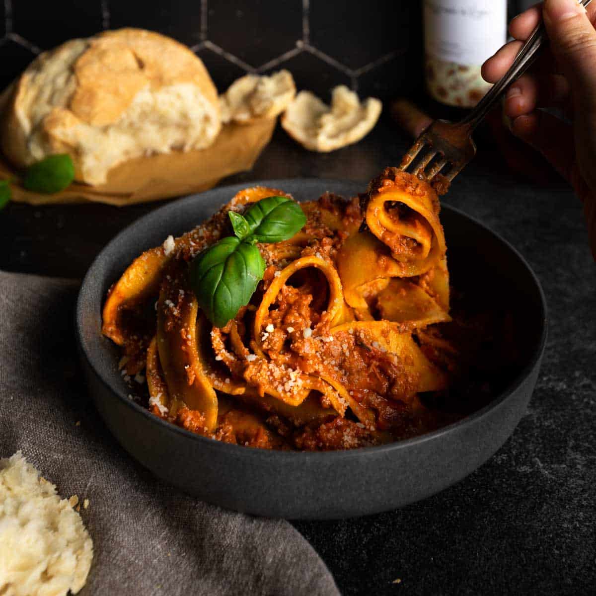 A fork lifting a twirled bite a pappardelle pasta covered in Beef Bolognese 