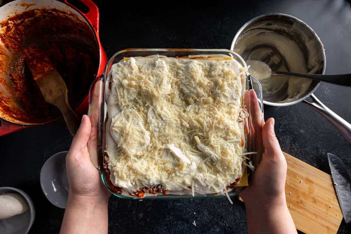 Hands holding an unbaked authentic Italian lasagne topped with Parmesan béchamel, fresh mozzarella and shredded Parmesan cheese