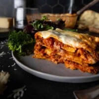 A big slice of Lasagna Bolognese on a plate with a green salad
