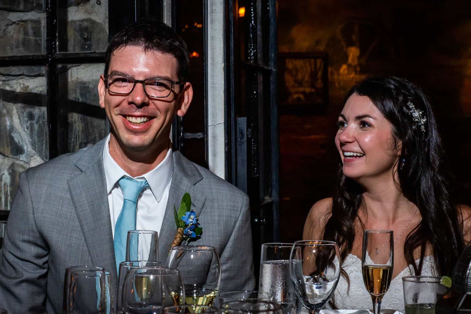 Scott and Taylor Woodworth at a table full of wine glasses at their wedding dinner. 