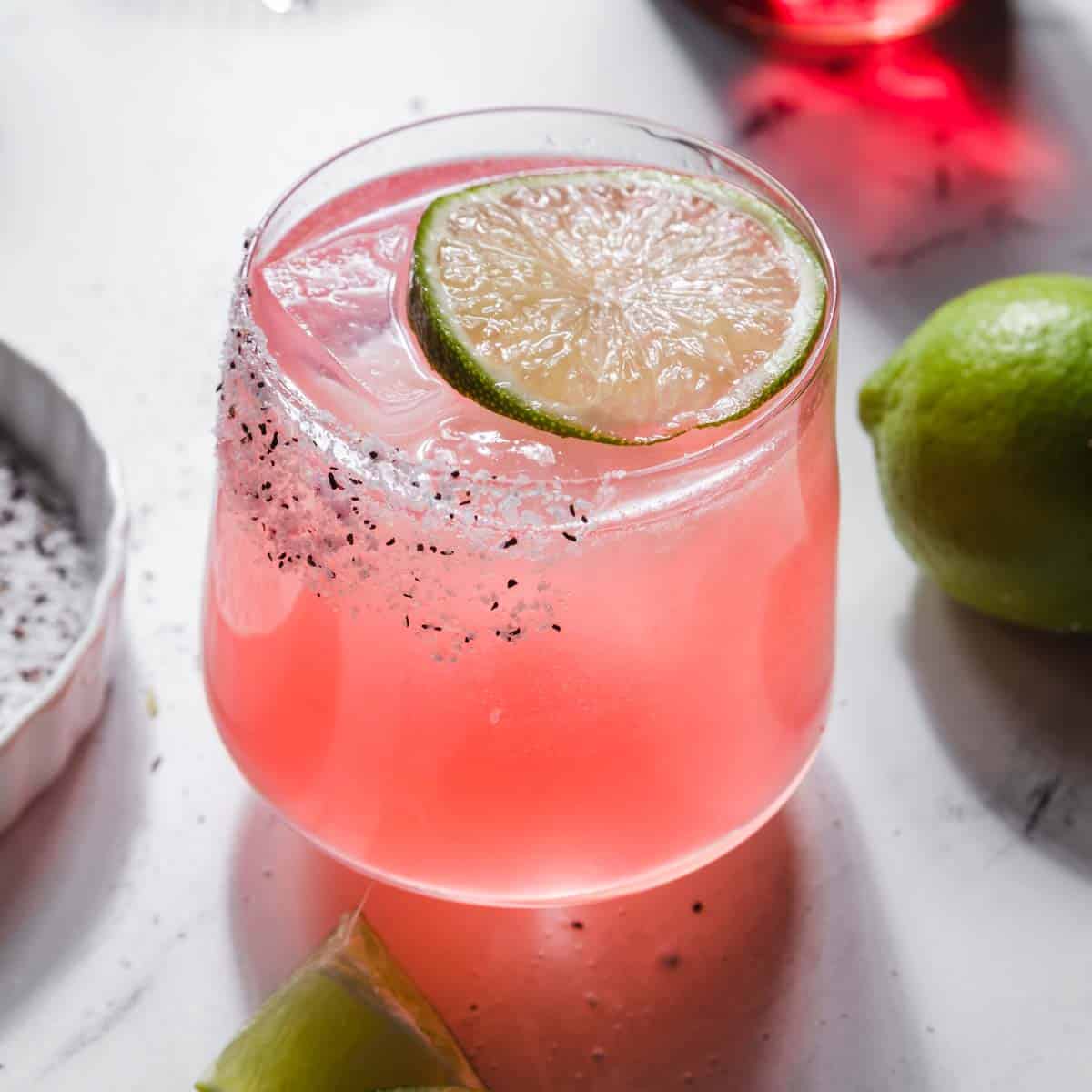 A glass of pink hibiscus margarita on the rocks with a floating lime wheel garnish
