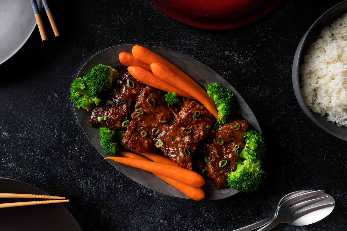 A platter of Korean short ribs served with white rice, carrots broccoli and scallion