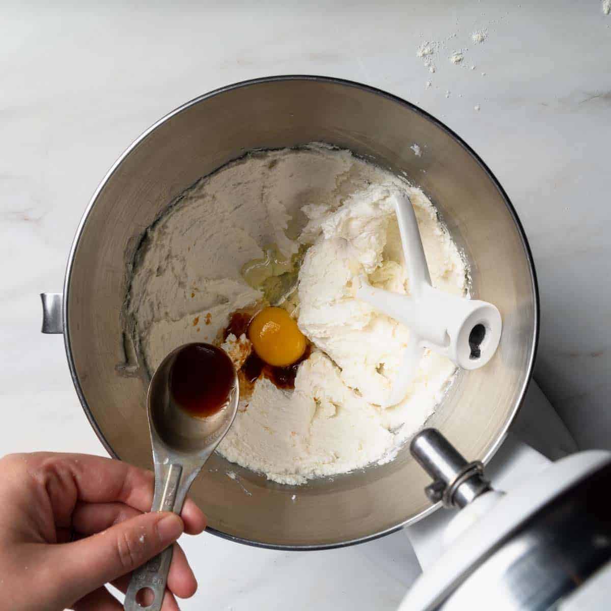Adding vanilla extract to the stand mixer with creamed butter and sugar and a whole egg