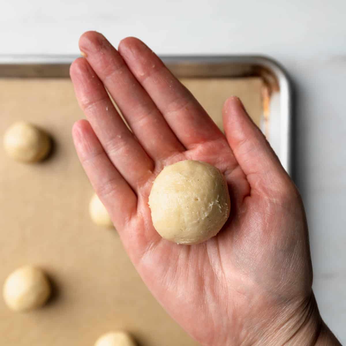 A hand holding a small ball of rolled cookie dough