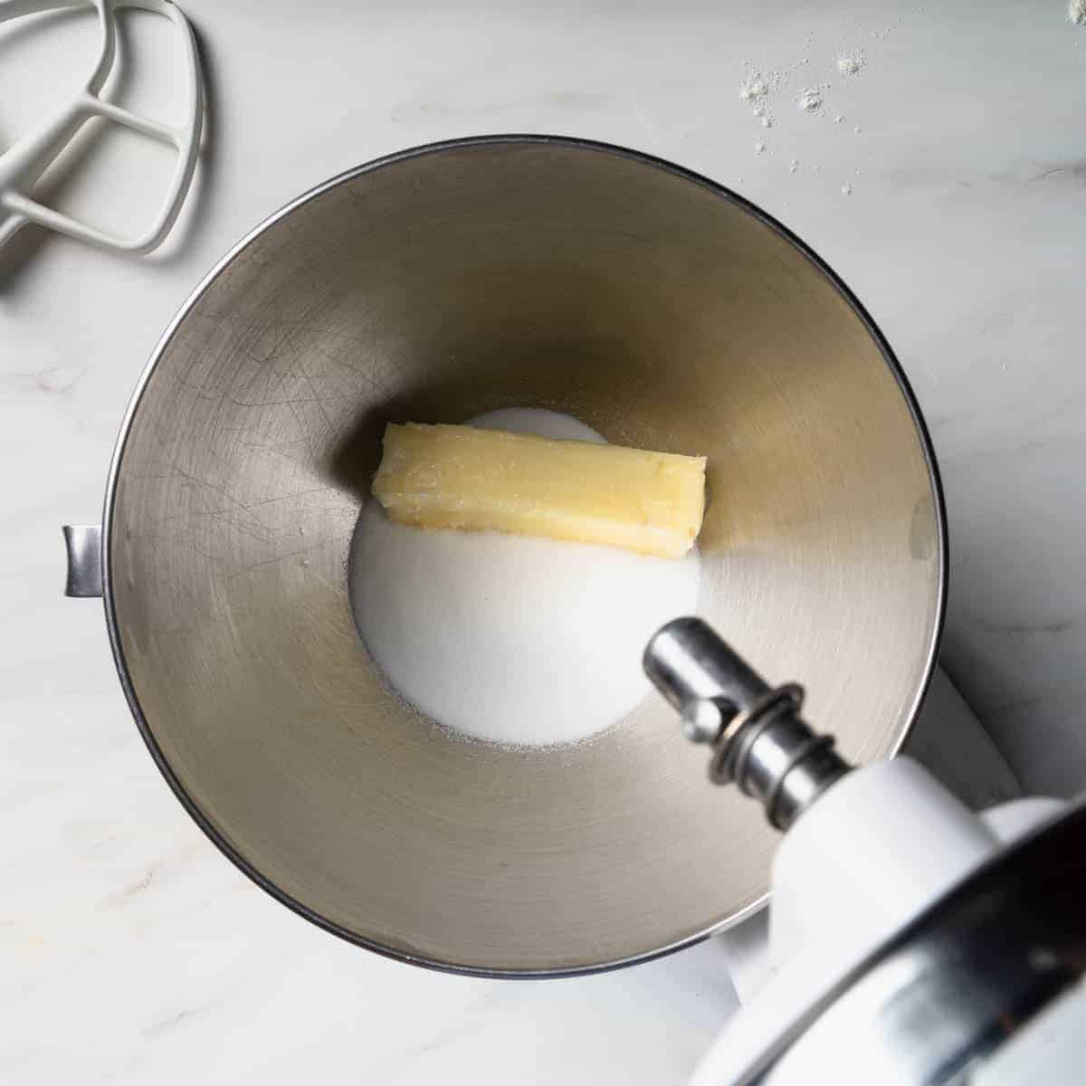 The bowl of a stand mixer with sugar and a soft stick of butter