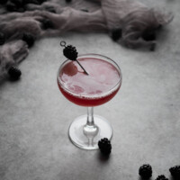 A blackberry bee's knees cocktail in a coupe