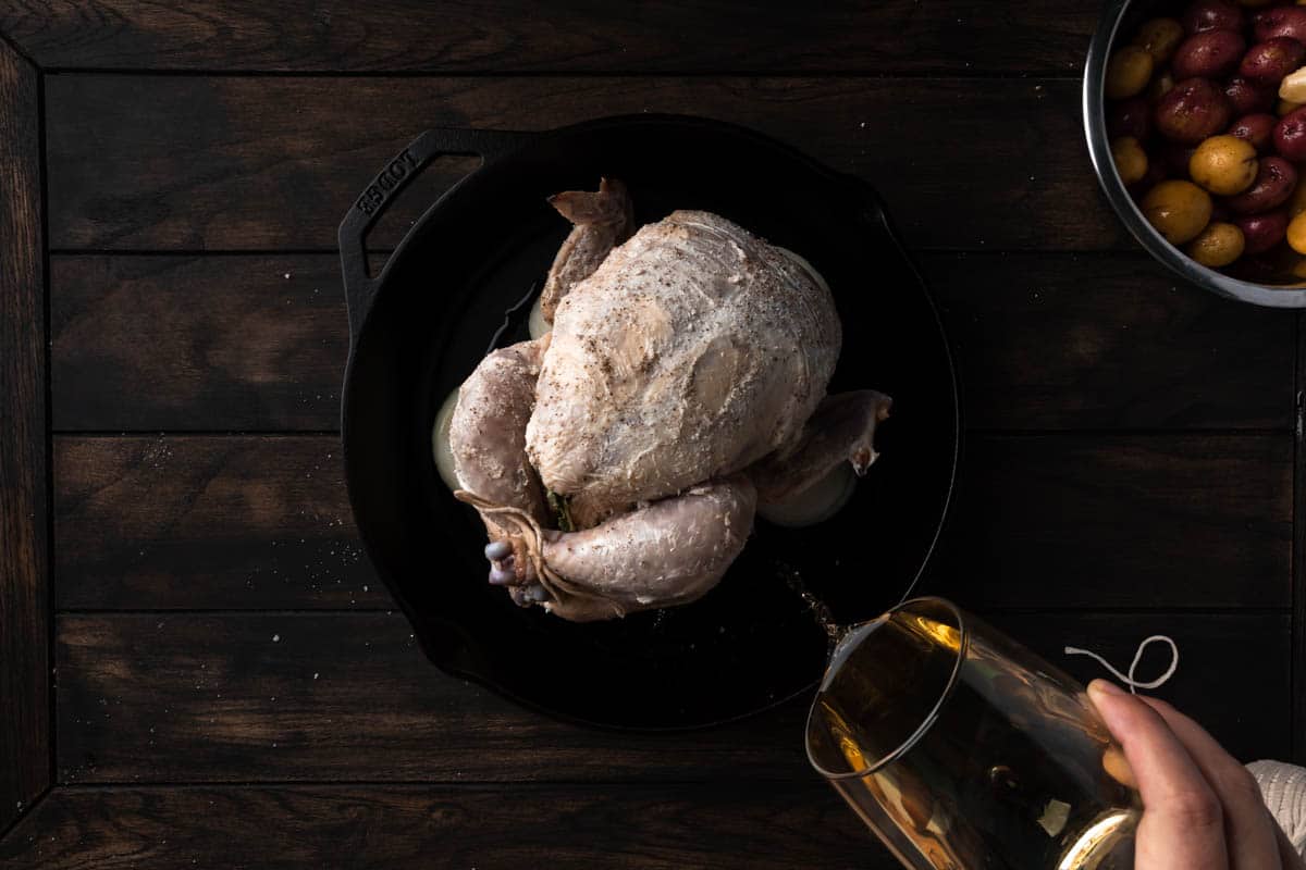 Pouring white wine into the skillet around the chicken