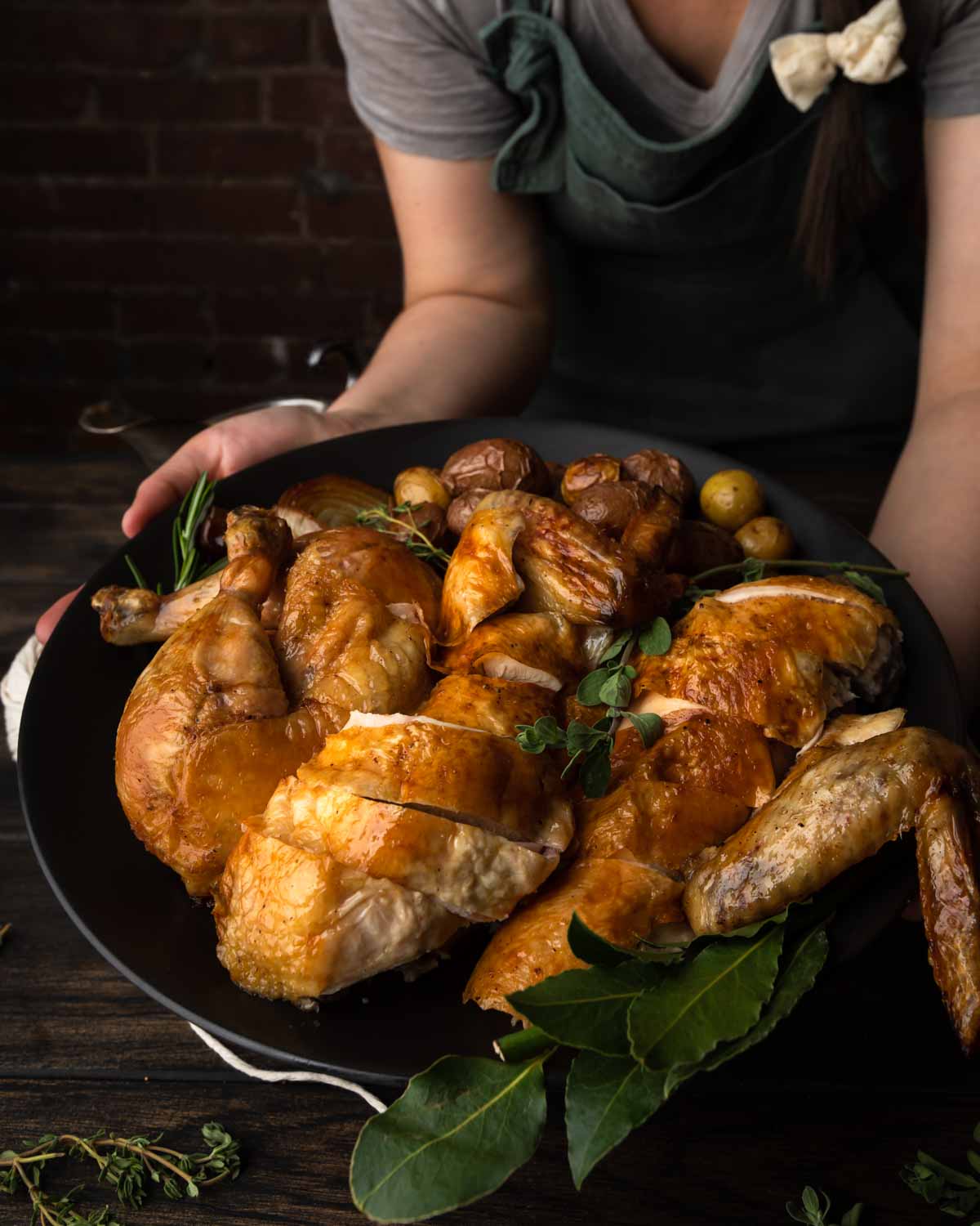 A woman holding a platter of carved roast chicken and baby potatoes.