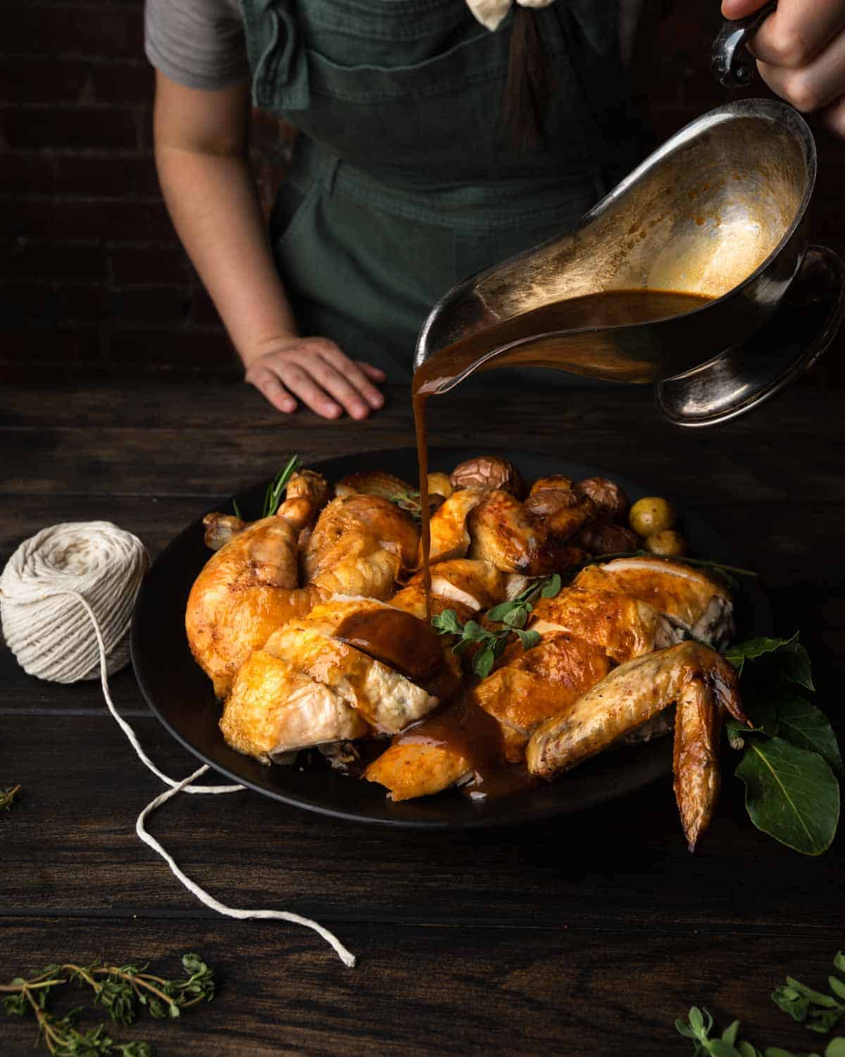 Pouring white wine pan sauce over a platter of cast iron roast chicken.