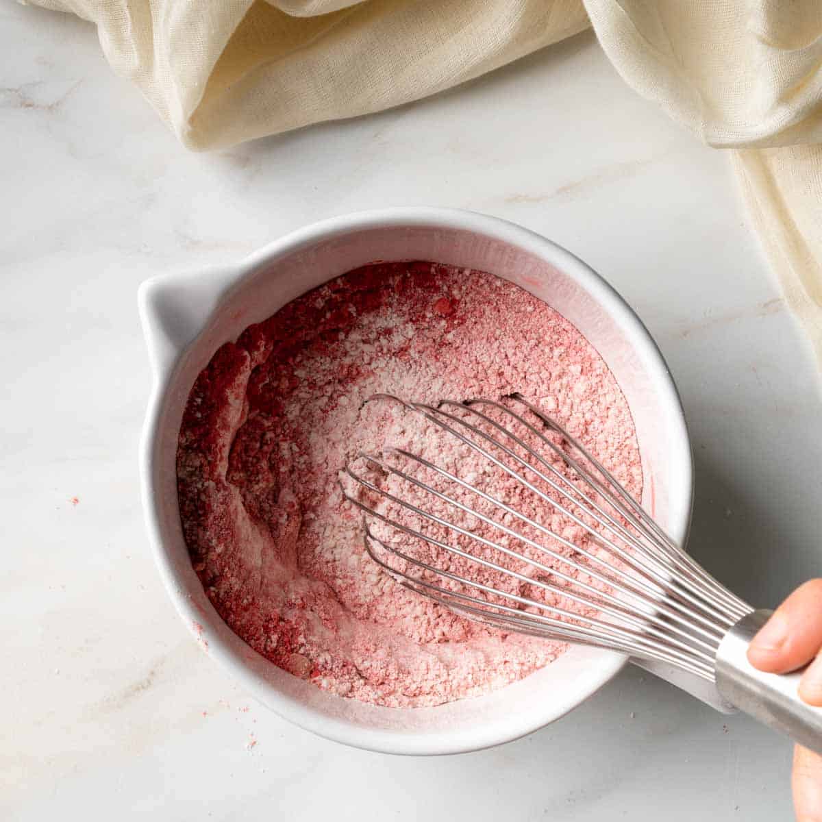Whisking the pink strawberry flour mixture together in a white mixing bowl