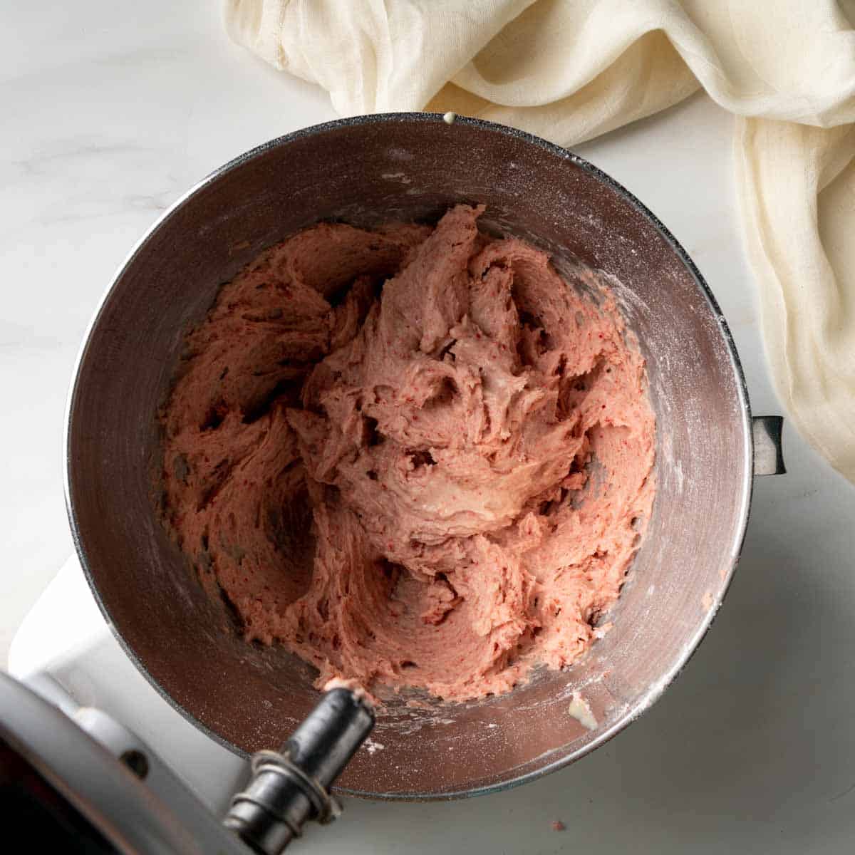 A thick pink strawberry cake batter in the bowl of a stand mixer