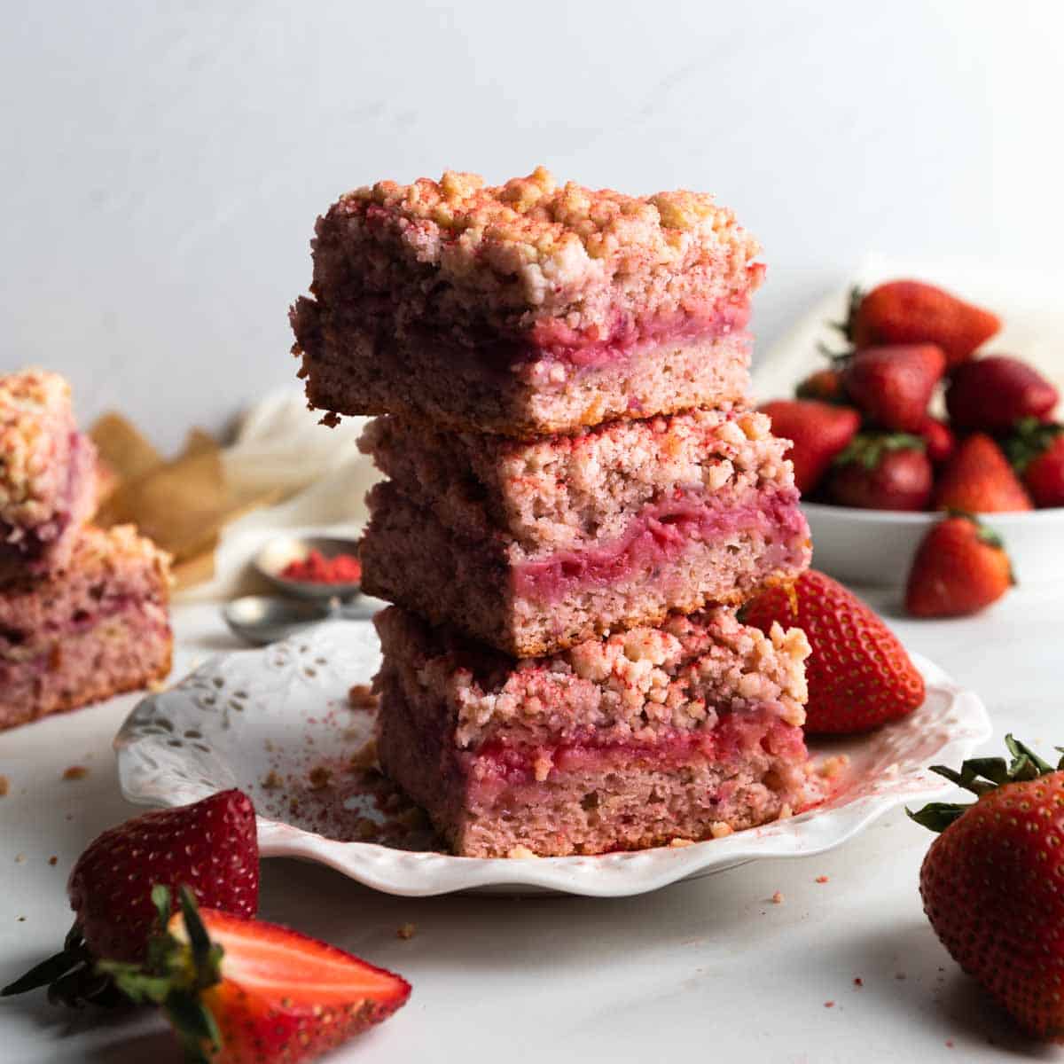 A stack of square slices of strawberry crumb cake and fresh strawberries