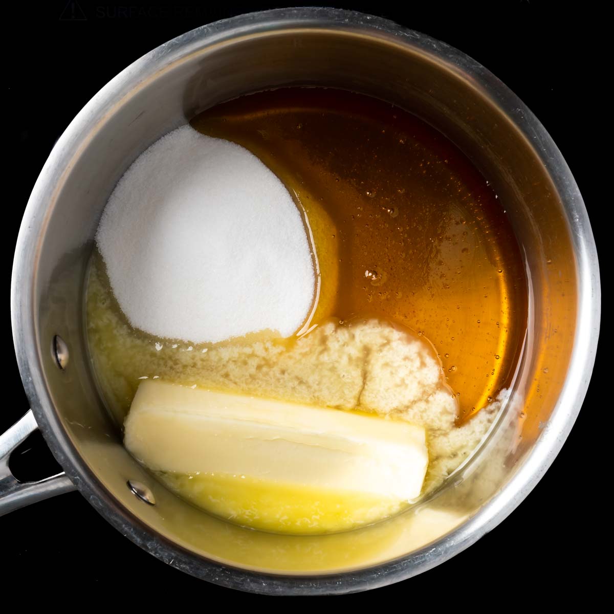 A stick of butter melting in a pot with sugar and honey