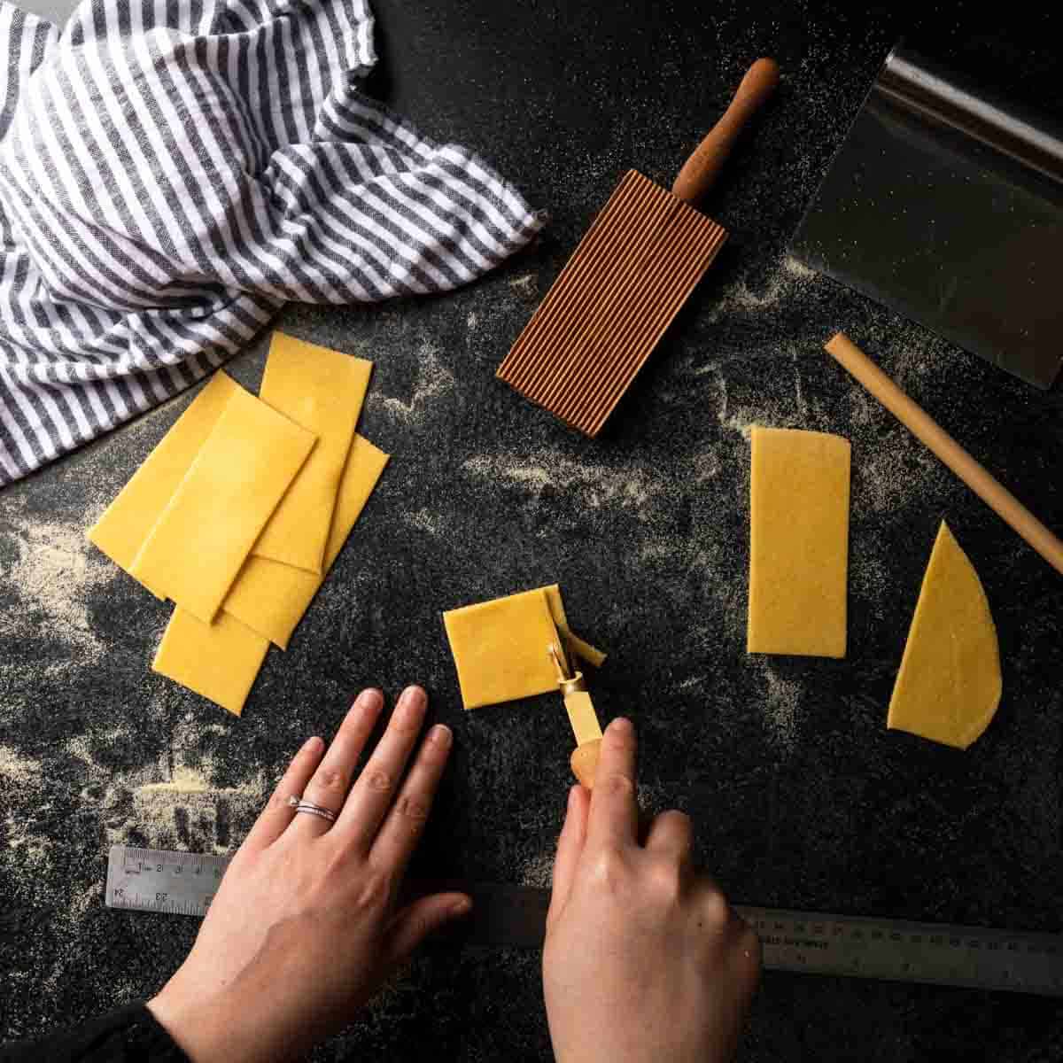 Using a ruler and brass pasta wheel to cut squares of pasta dough