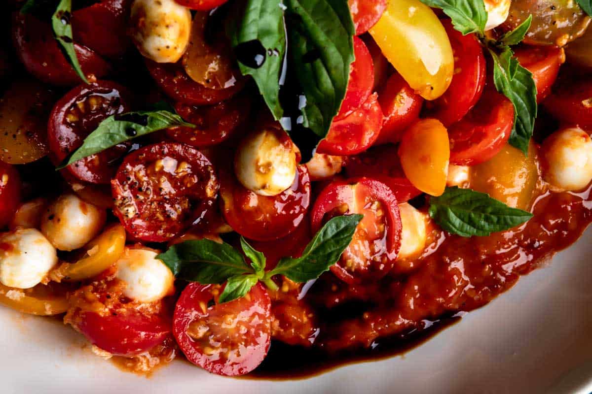 A close up image if cherry tomato caprese salad over roasted tomato vinaigrette