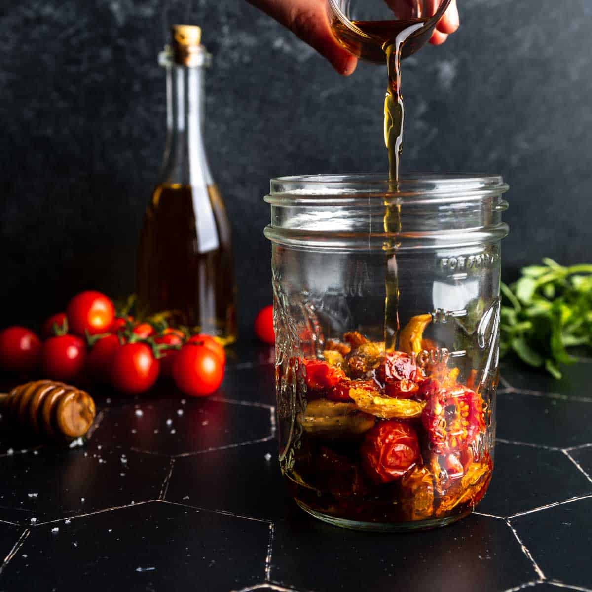 Pouring oil over a jar of roasted cherry tomatoes
