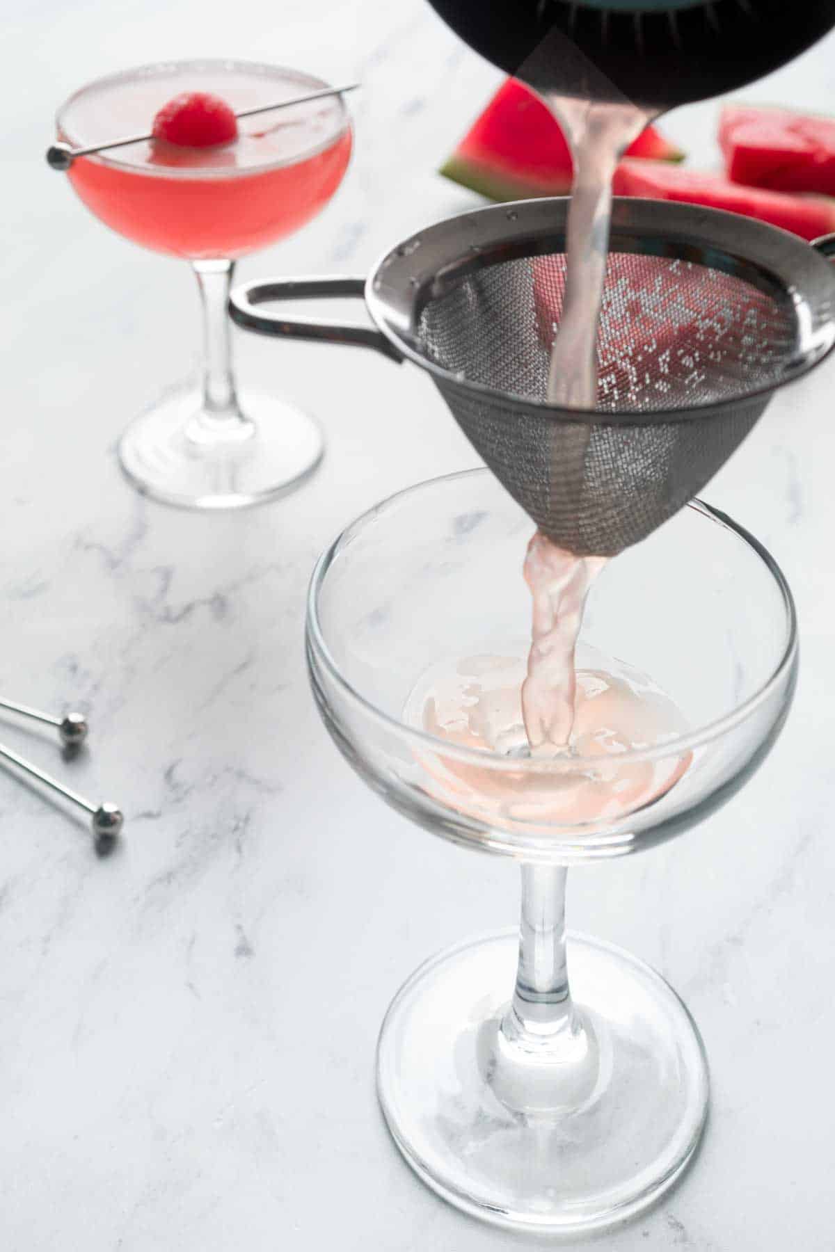 Straining a watermelon vodka cocktail into a martini glass