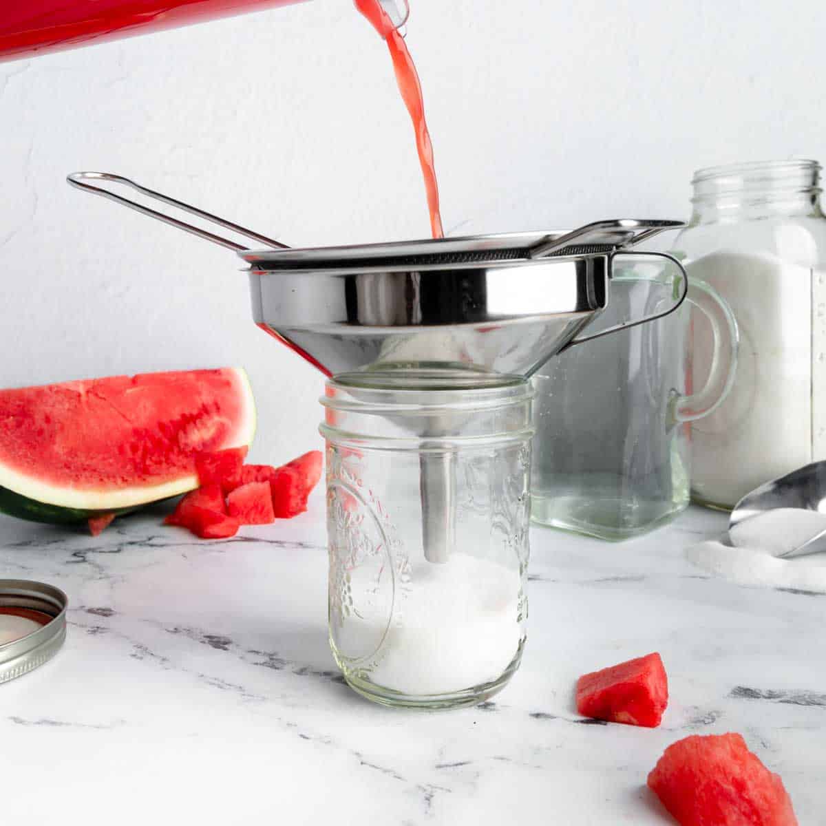 Straining watermelon puree into a jar with sugar