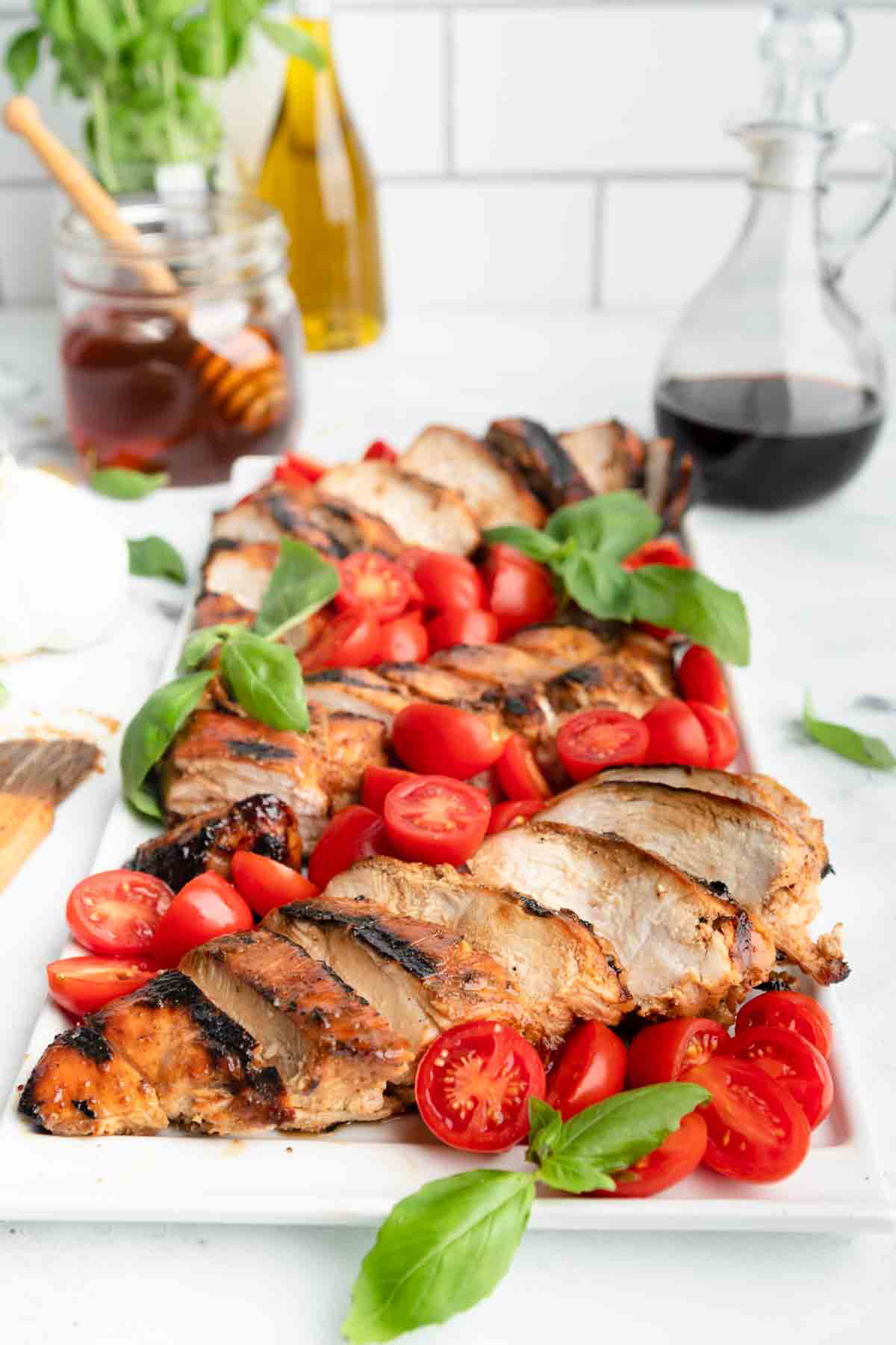 A big platter of grilled honey balsamic chicken with cherry tomatoes and basil