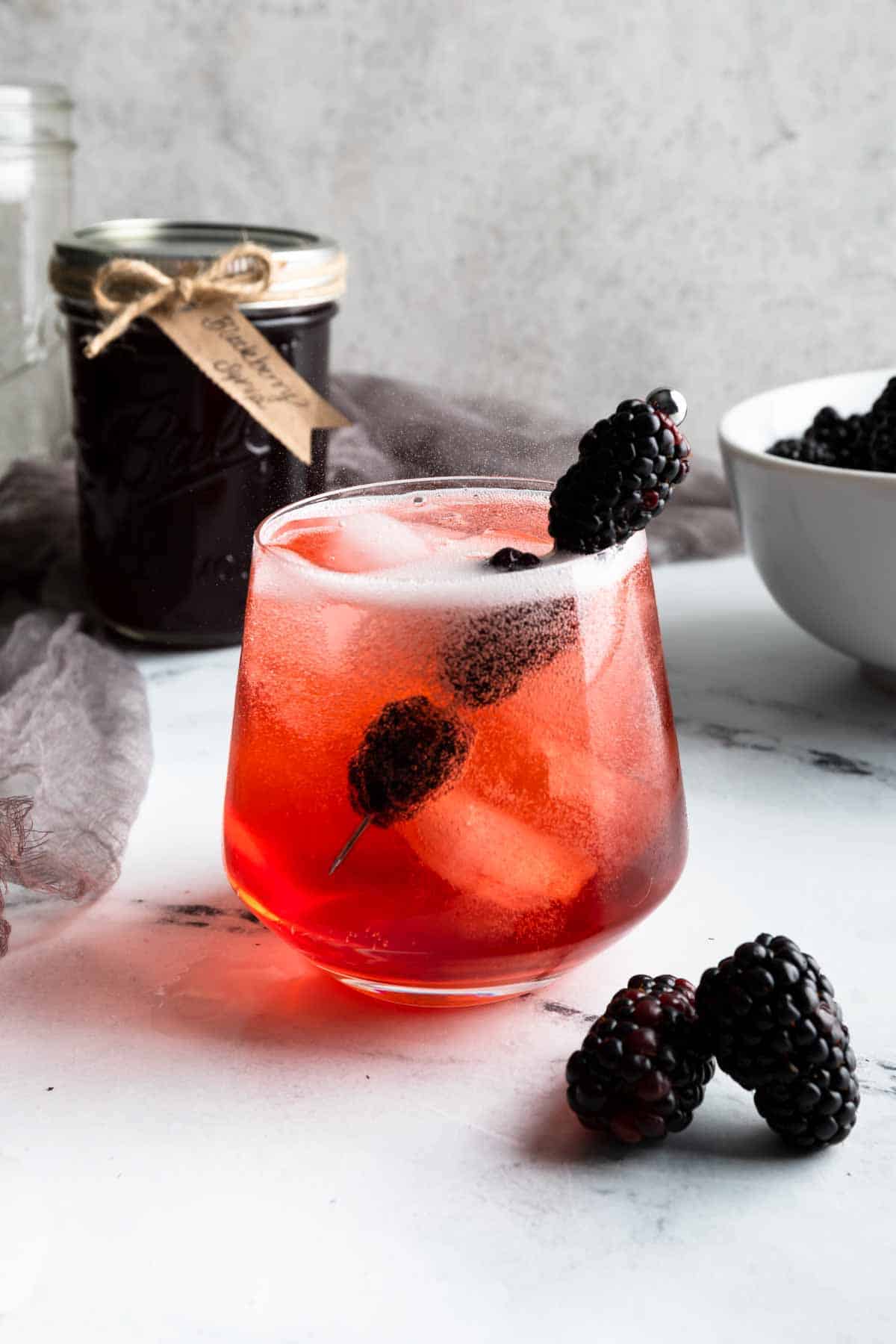 A glass filled with a blackberry Shirley temple and fresh berries